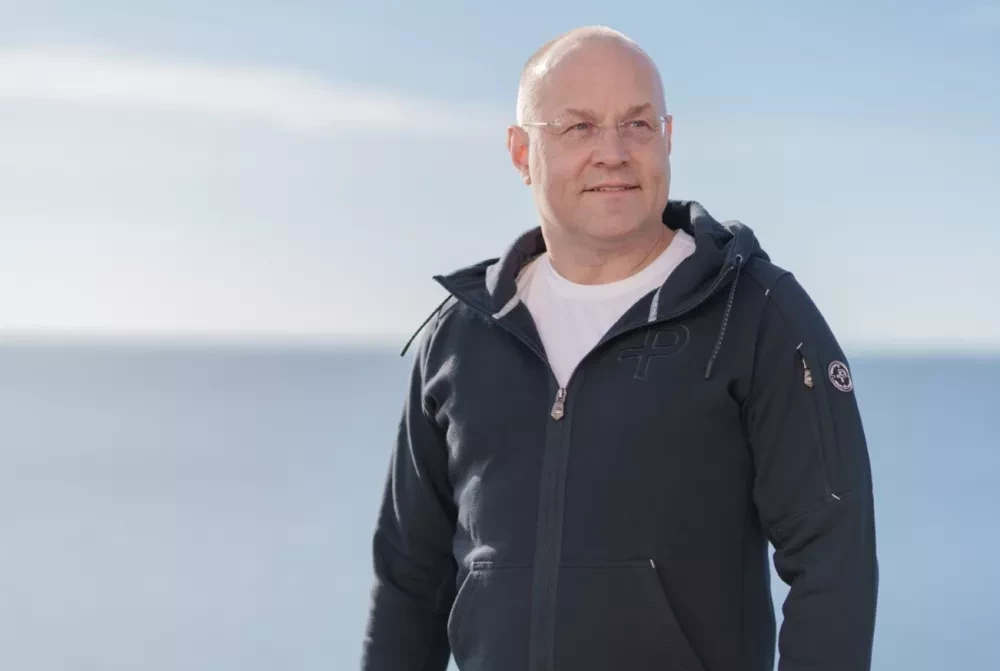 Man in white t-shirt and blue hoodie in front of ocean